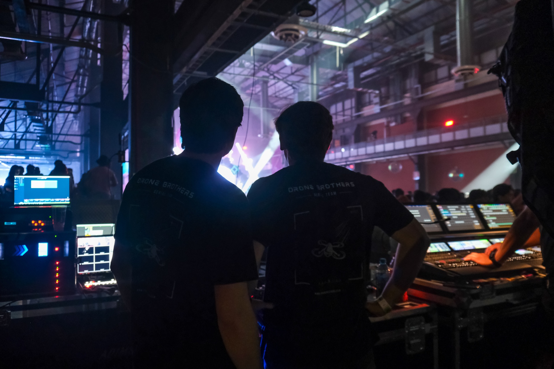Two Drone Brothers operators at the FOH console as the stage flashes cool blue and white