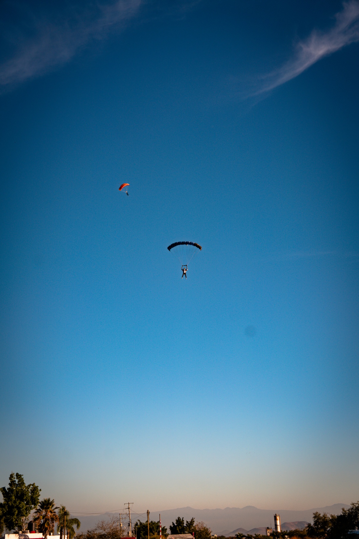 Two skydivers descending under open canopies against a deep blue sky