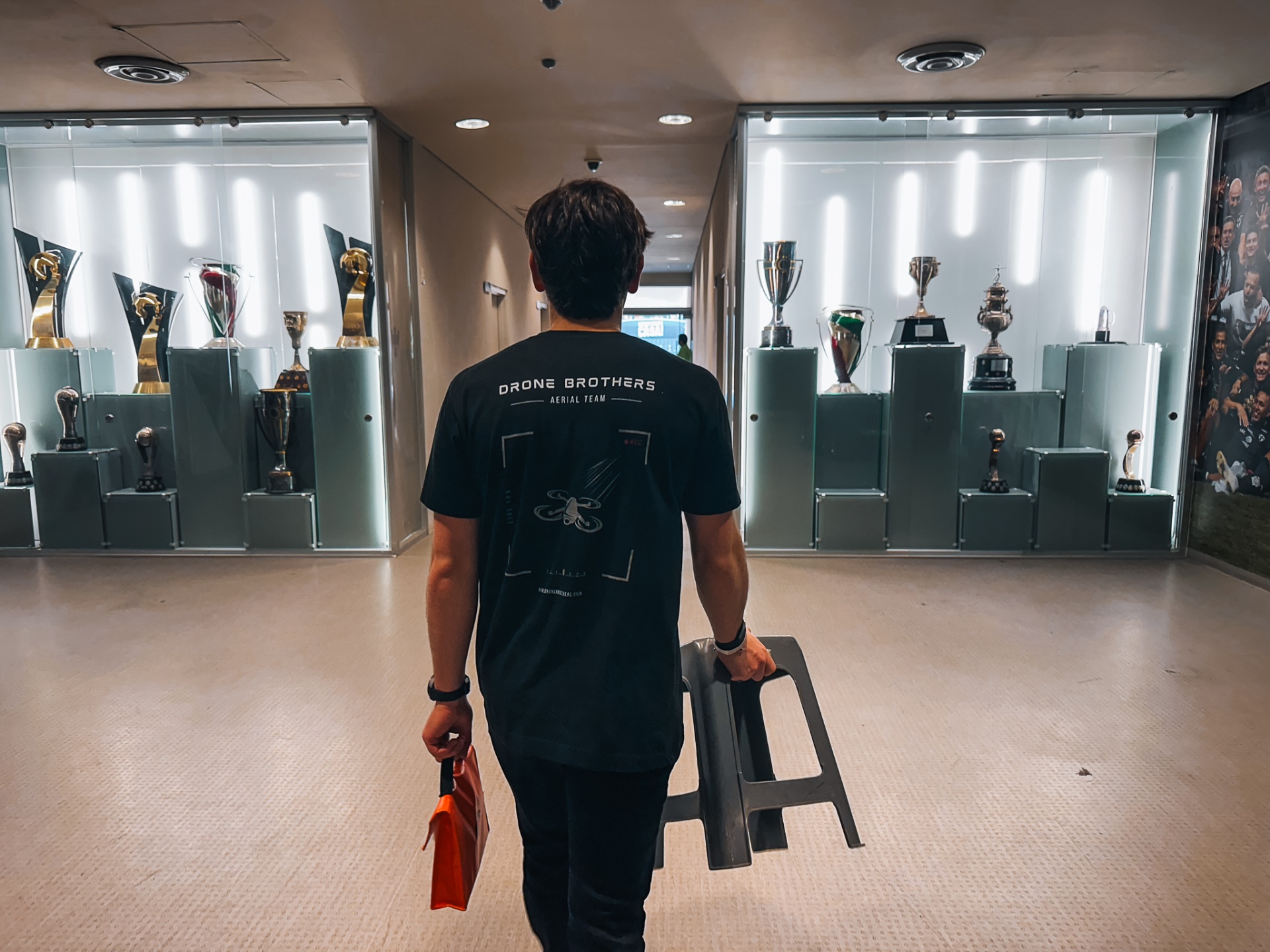 Dronebrothers operator in branded tee walking through Rayados trophy hall at Estadio BBVA