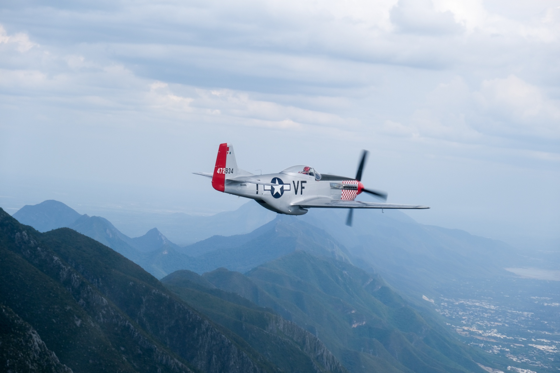 Silver P-51 Mustang banking through clouds above the Sierra Madre