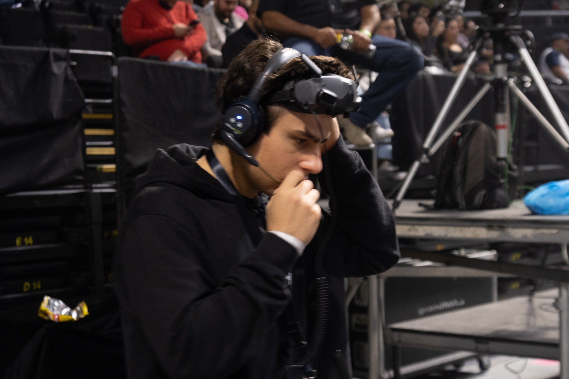 FPV pilot inside an arena wearing intercom headset with DJI goggles pushed up on his forehead