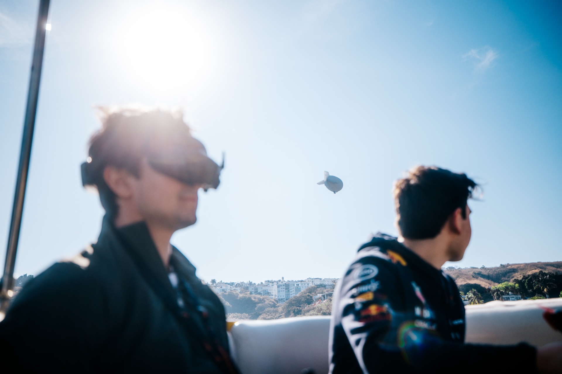 FPV pilot flying with goggles on a boat, blimp in the distance