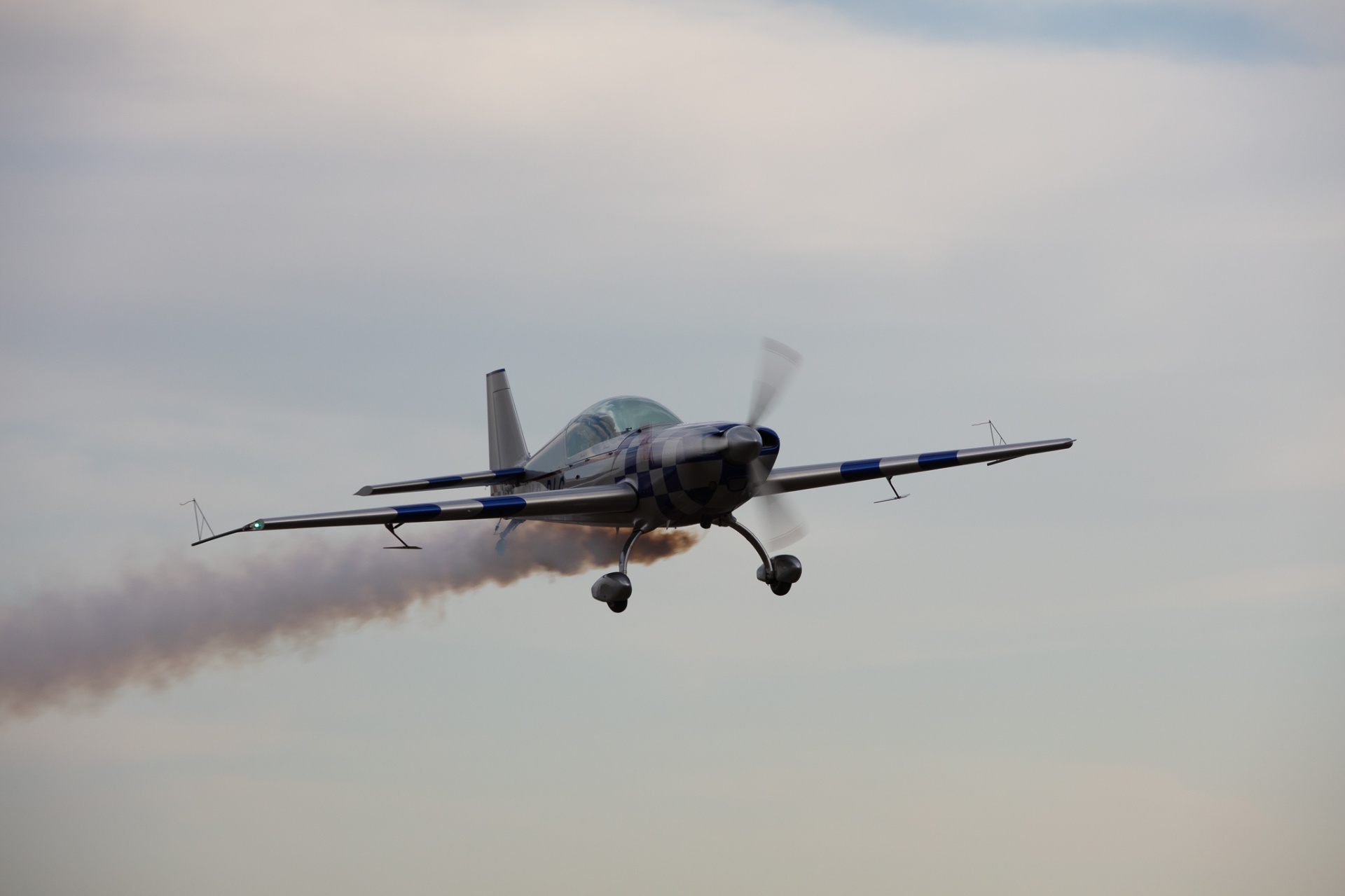 Checkered aerobatic aircraft passing low with red smoke trailing