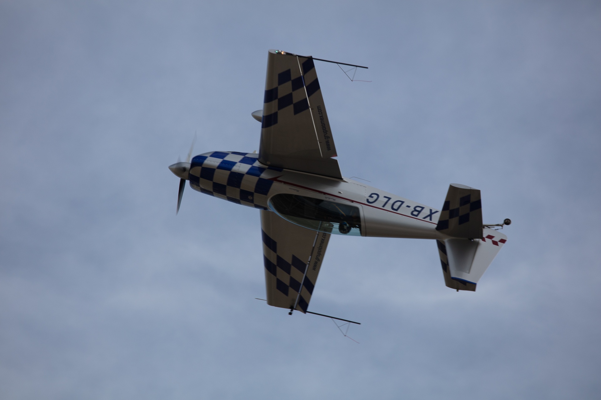 Top-down view of blue-and-silver checkered aerobatic plane in flight