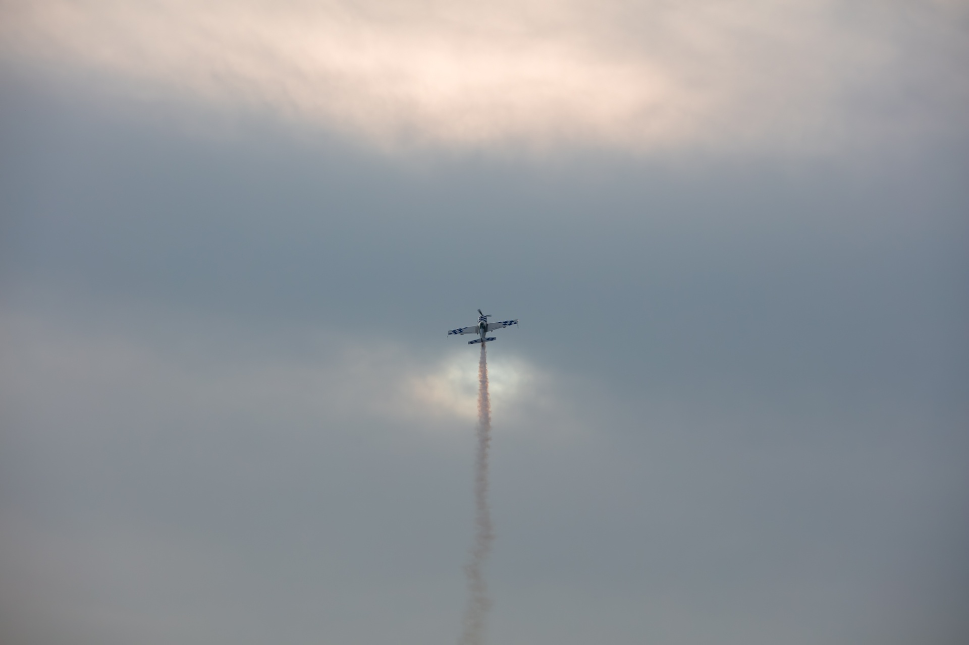 Aerobatic plane on a vertical climb piercing a cloud with red smoke