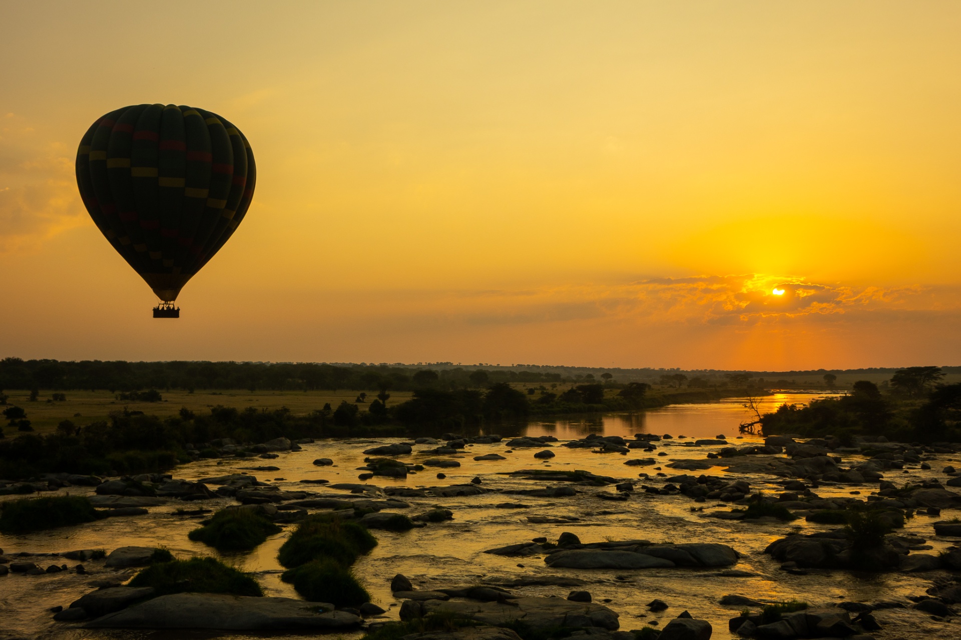 Hot air balloon drifting over a Serengeti river at sunrise