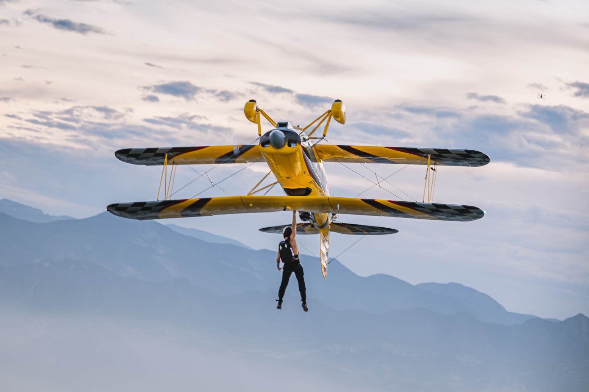 Wing walker hanging beneath yellow biplane over Monterrey sierra