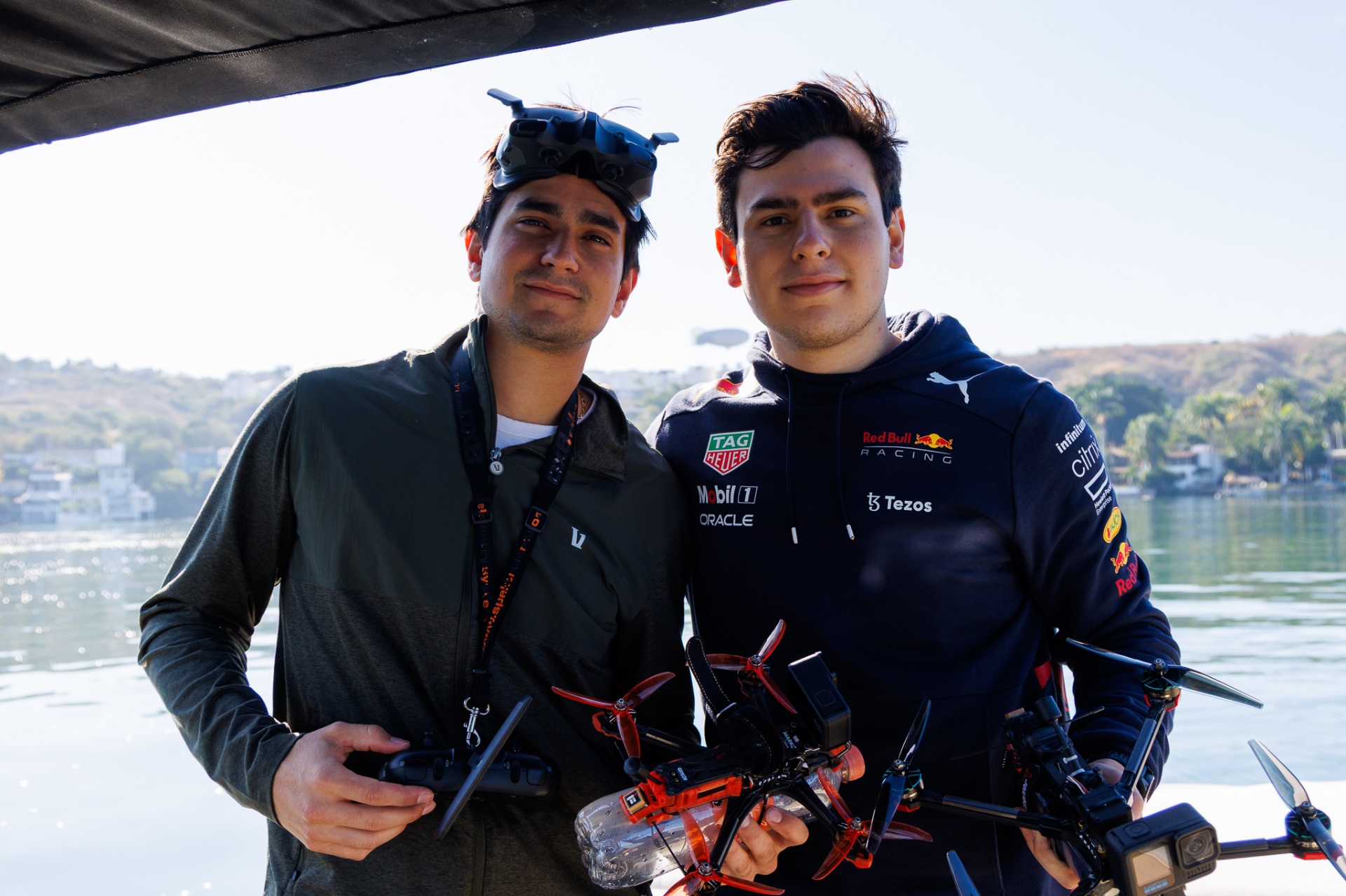 Two FPV pilots posing with cinelifters lakeside, one in Red Bull Racing kit