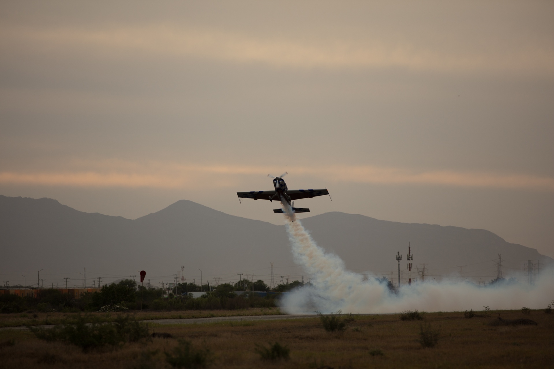 Aerobatic plane lifting off a runway at sunset with thick smoke trail