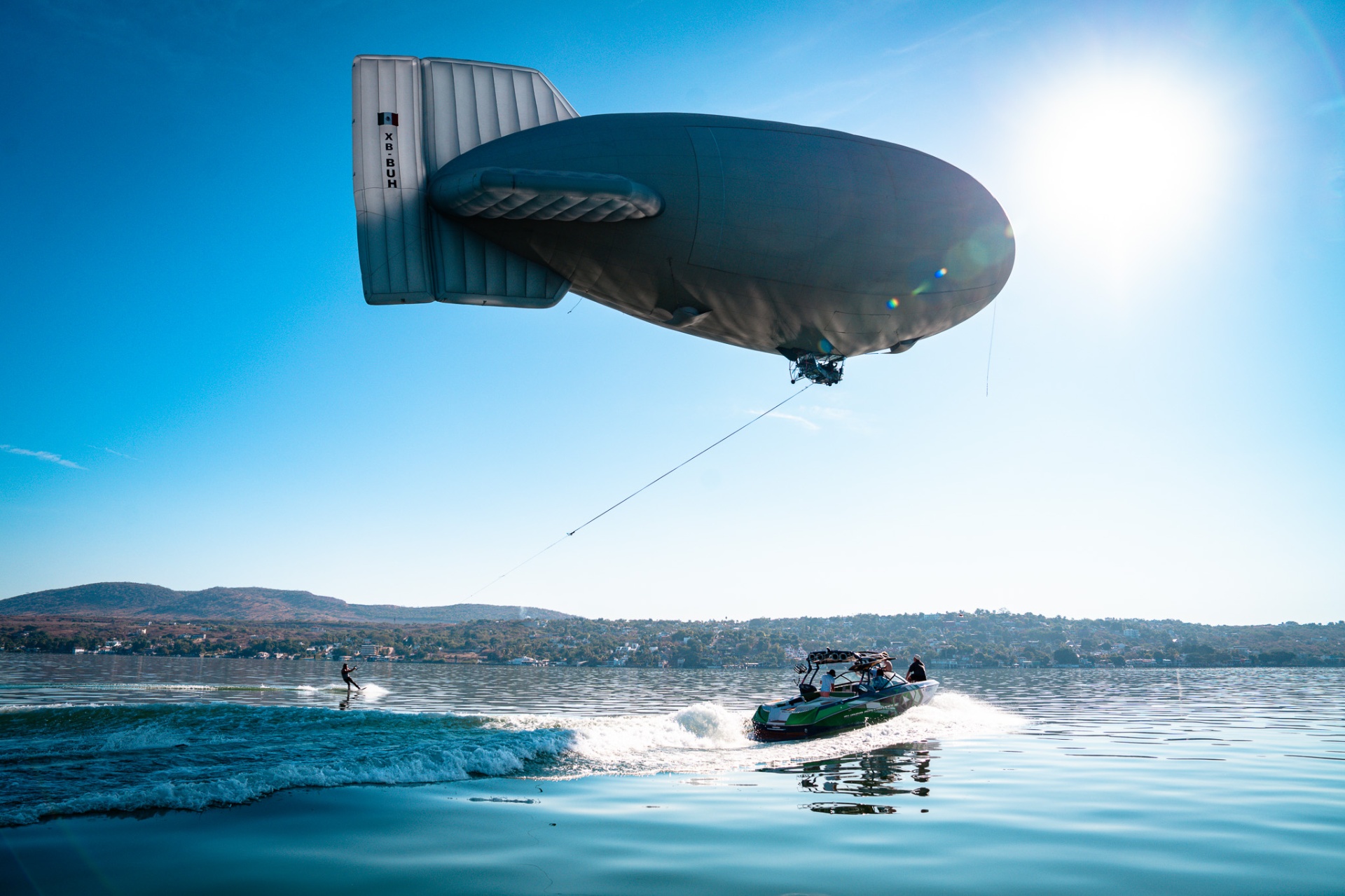 Tethered airship trailing a wakesurf boat across Lake Chapala in the sun