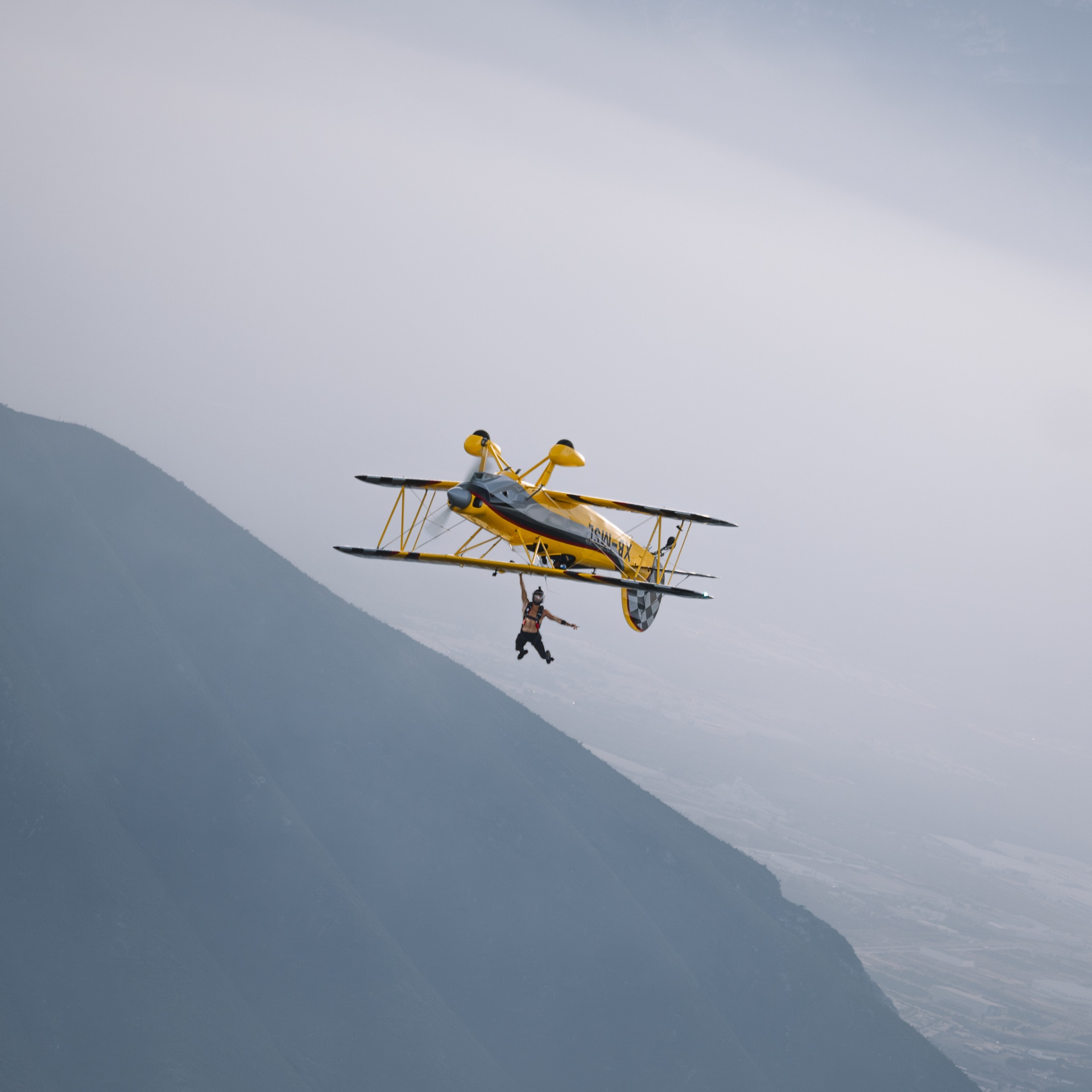 Wing walker dangling from biplane silhouetted against fogged ridge