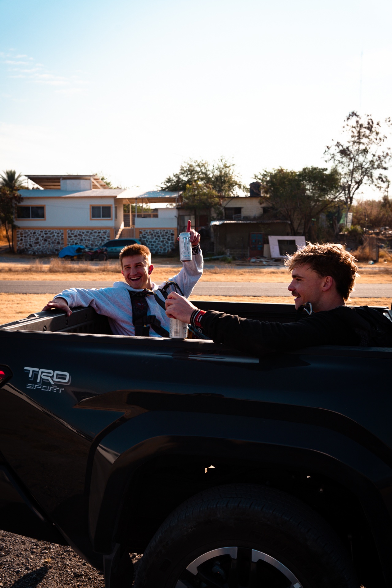 Two crew members laughing in the bed of a Toyota TRD pickup at golden hour